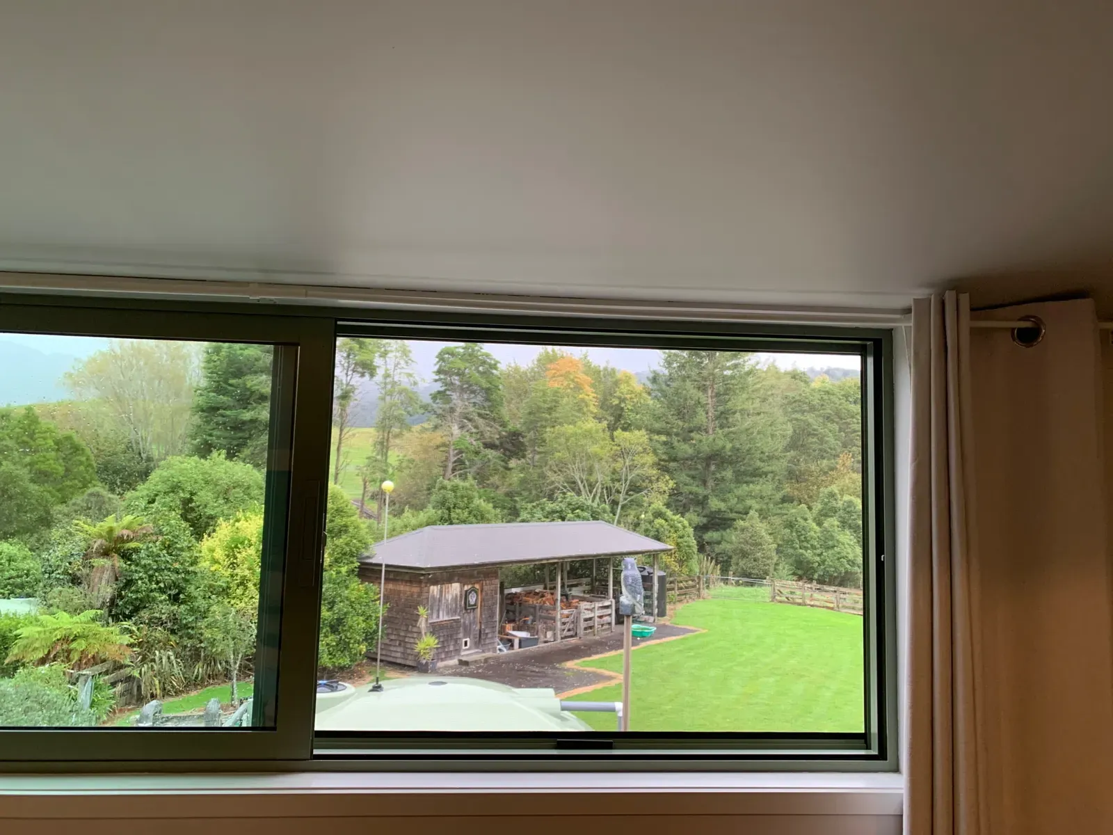 Serene retractable window screen over a picture window, framing a lush Ngongotahā Valley garden and bush