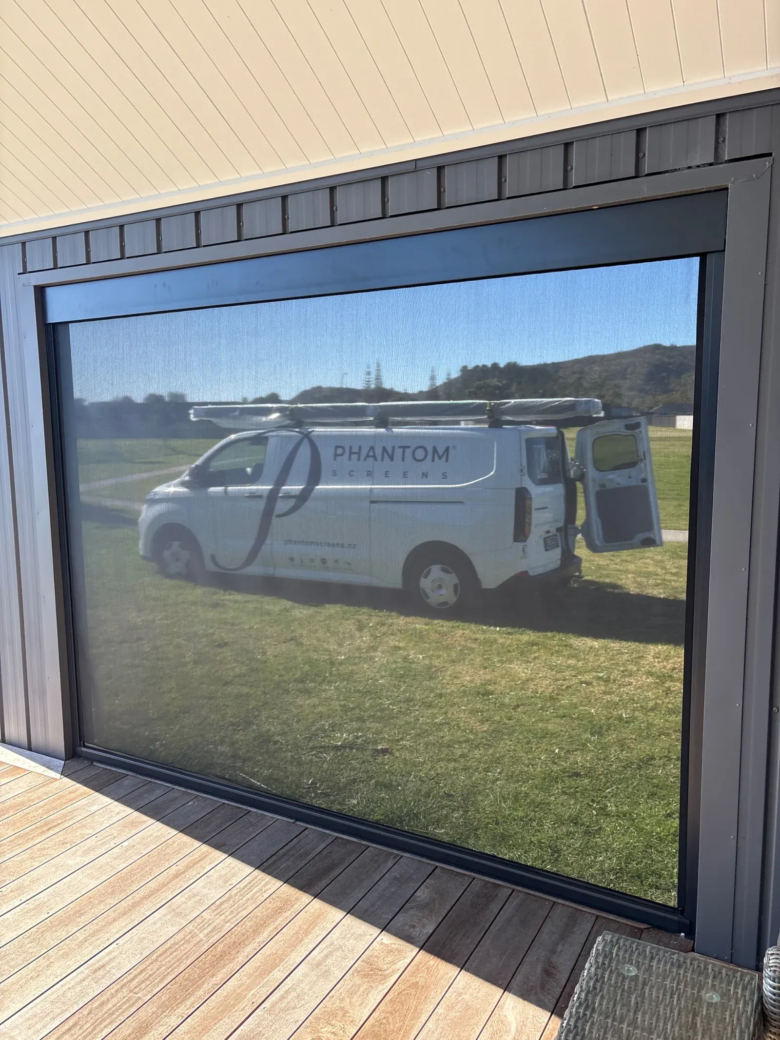 Charcoal Ziptrak outdoor blind lowered across a covered deck opening, a van and lawn clearly visible through the mesh