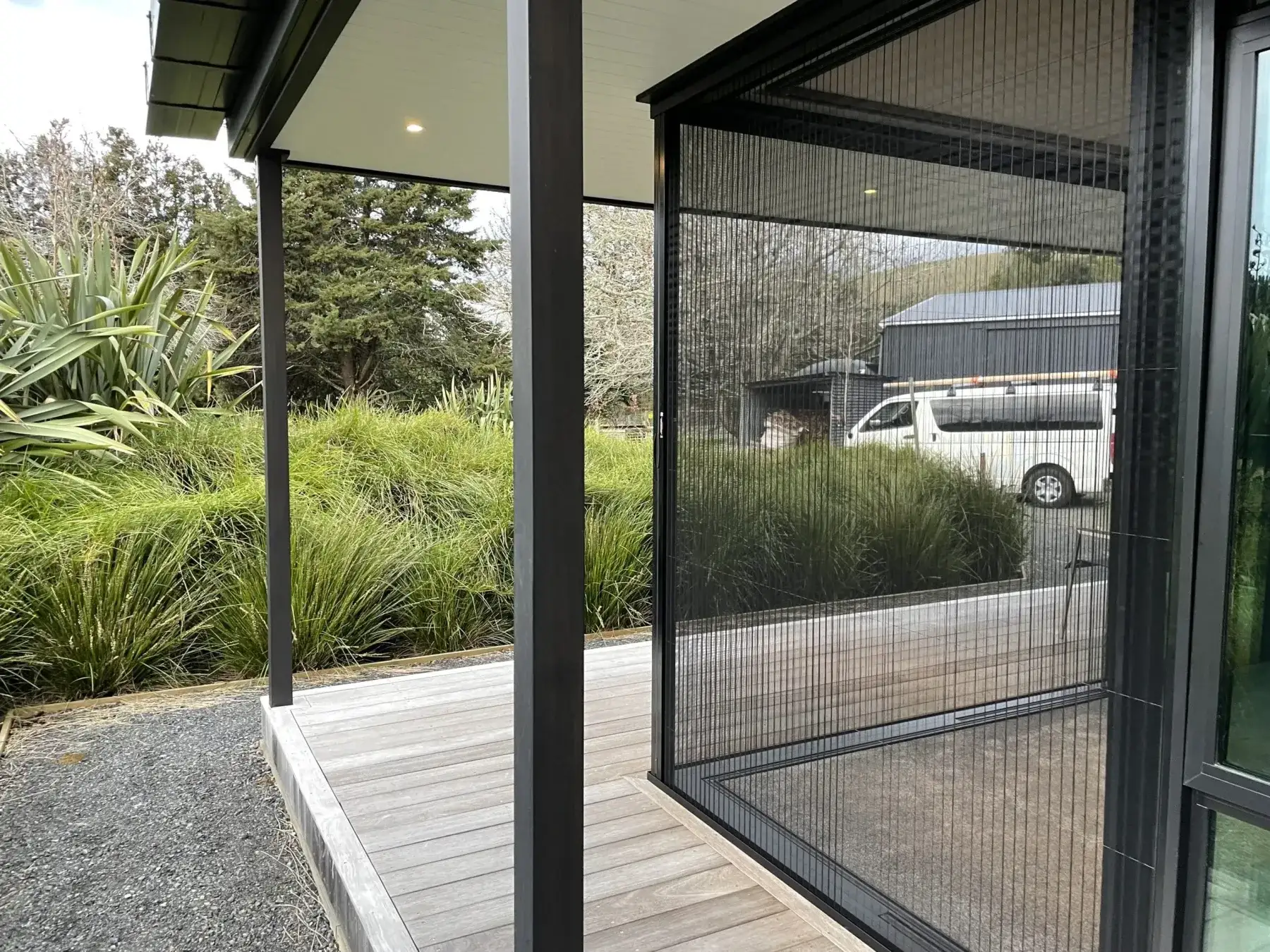 Dark-framed retractable pleated screens fitted around a corner deck opening of a New Zealand home