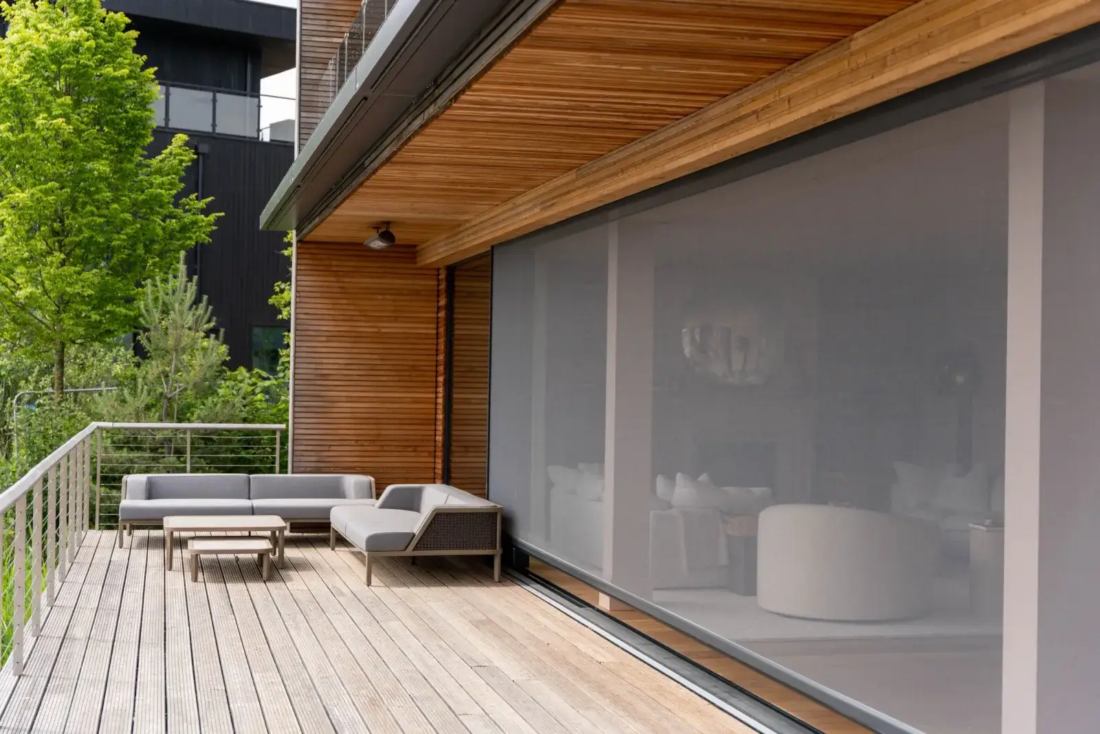A retractable outdoor screen drawn across a wide covered deck opening, under a timber-lined ceiling