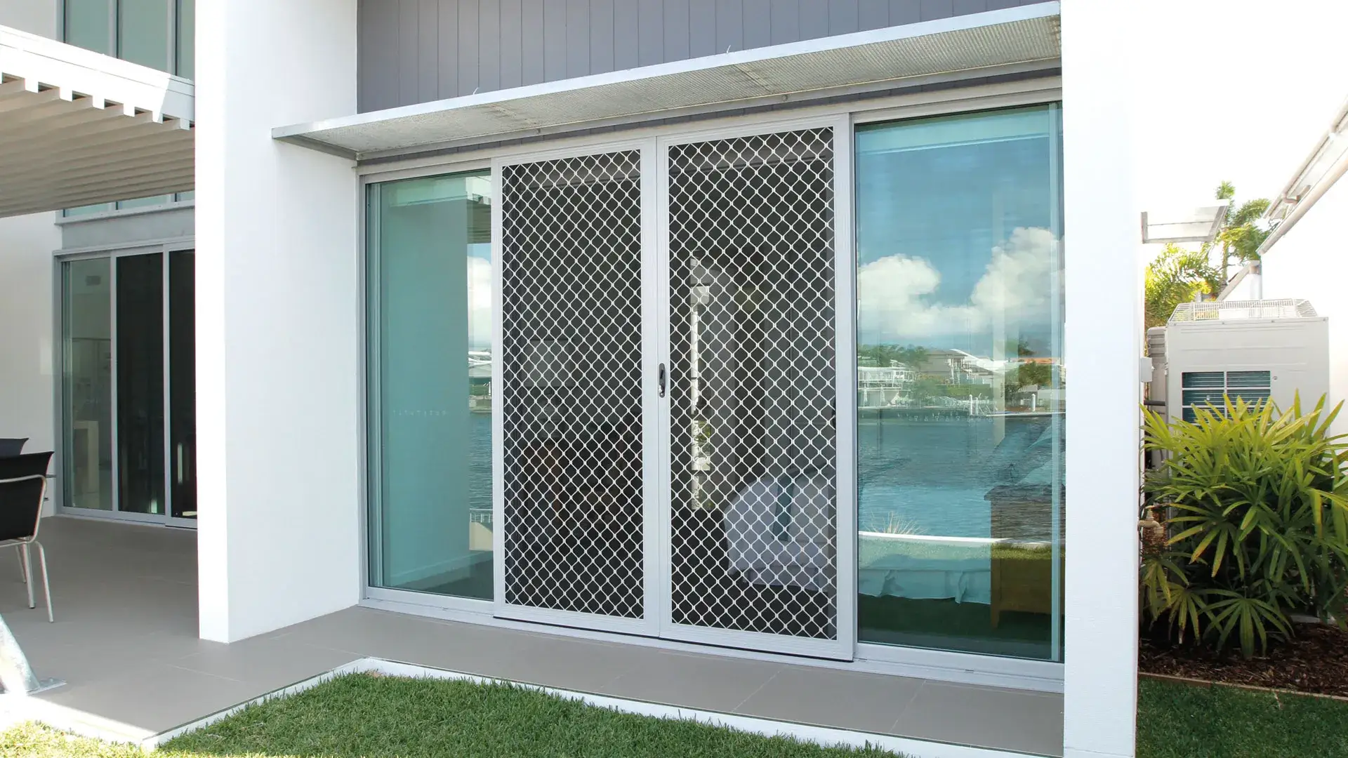 A LiveSafe aluminium security screen door with a diamond grille on a modern waterfront home