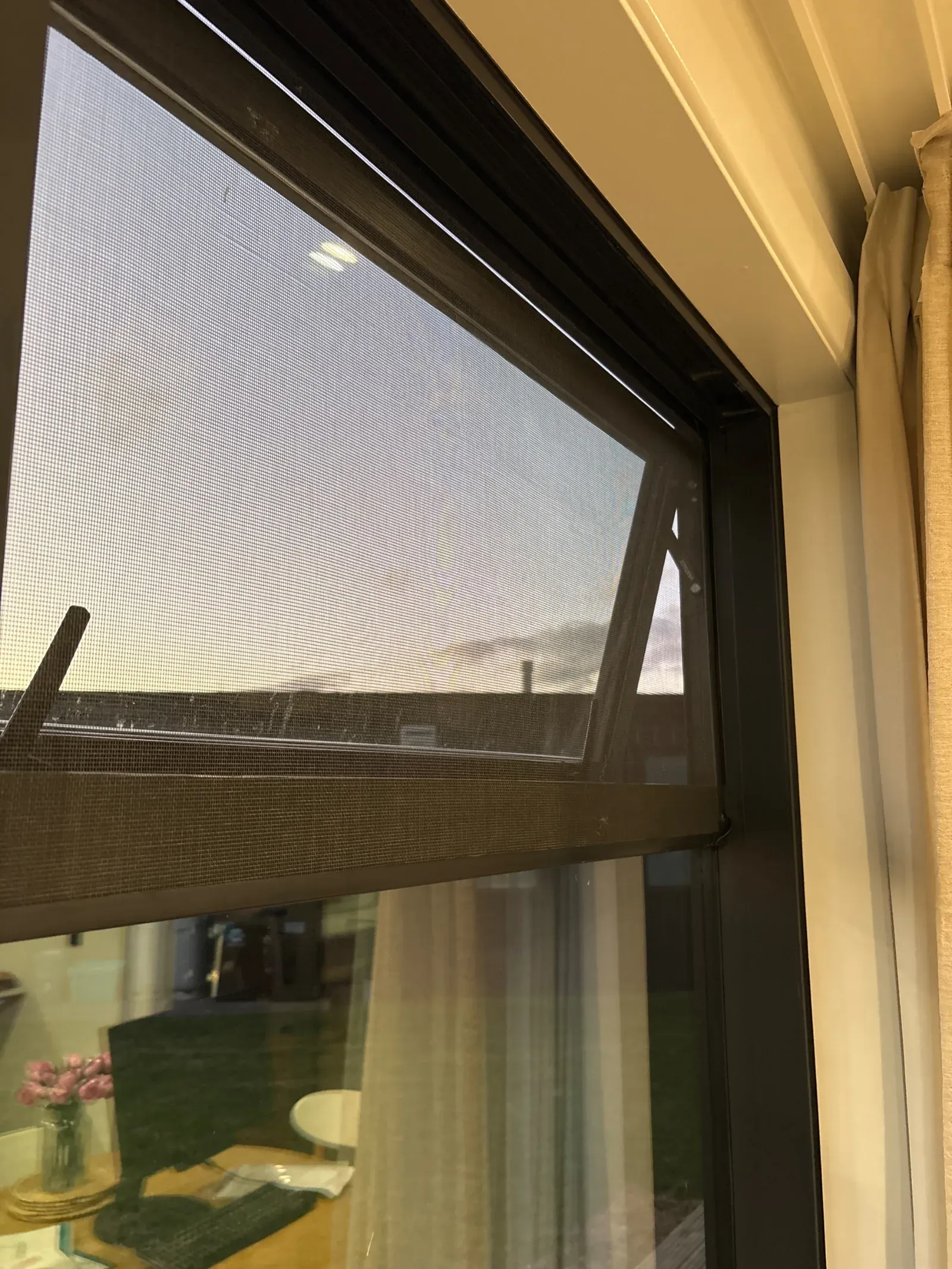 Black magnetic insect screen panel fitted over the opening top sash of a window, the awning pane wound open behind the flat mesh