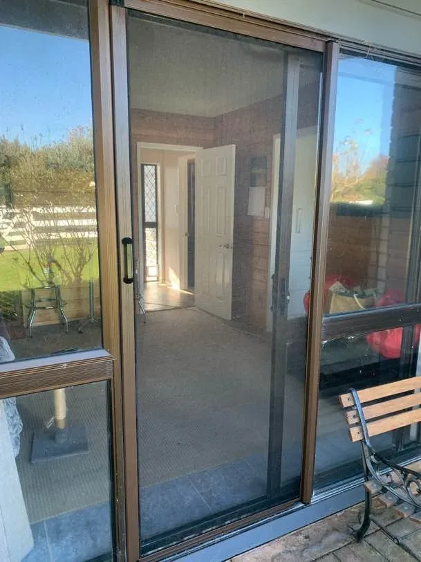 A pleated retractable door screen pulled across a timber-framed slider, looking into a sunlit family home