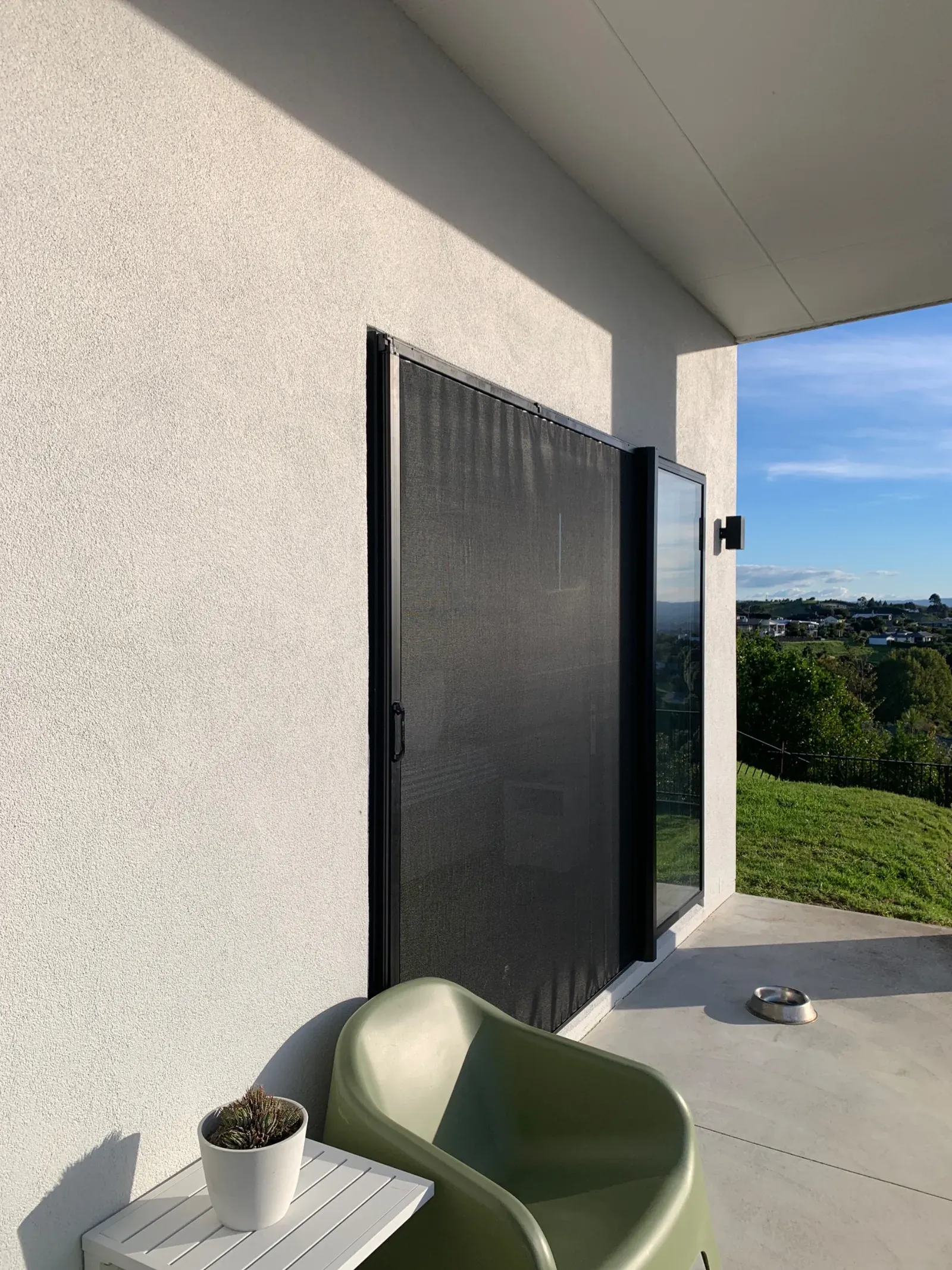 Black retractable screen pulled across a single sliding glass door on a modern home with a rural outlook