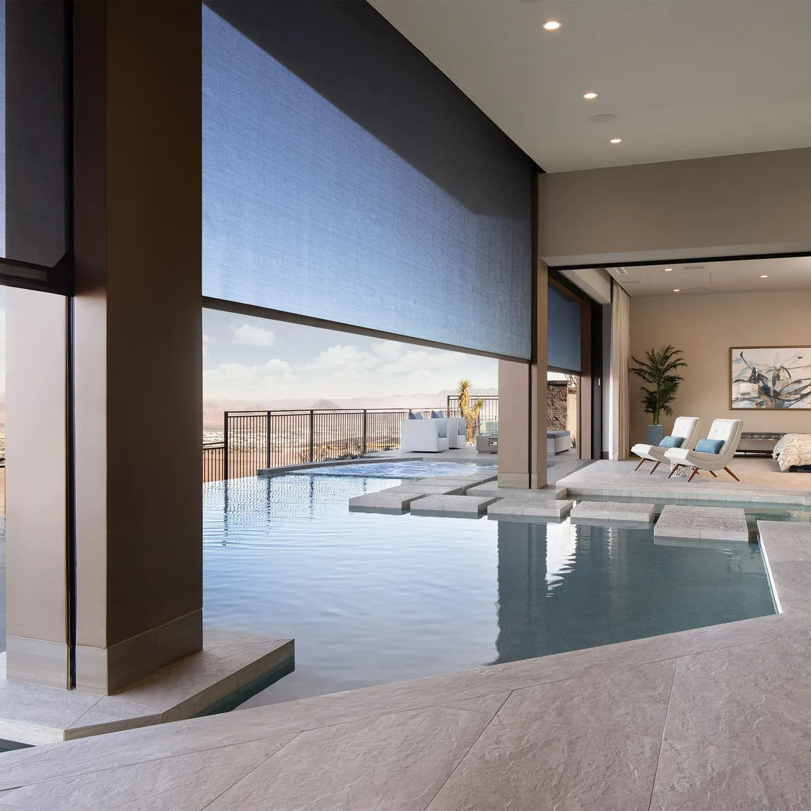 Motorised solar-mesh outdoor screen part-lowered over a covered poolside patio opening to an interior lounge