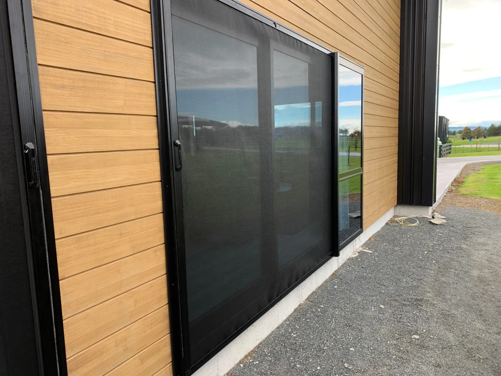 A wide black retractable screen drawn across a large sliding door on a timber-clad rural home