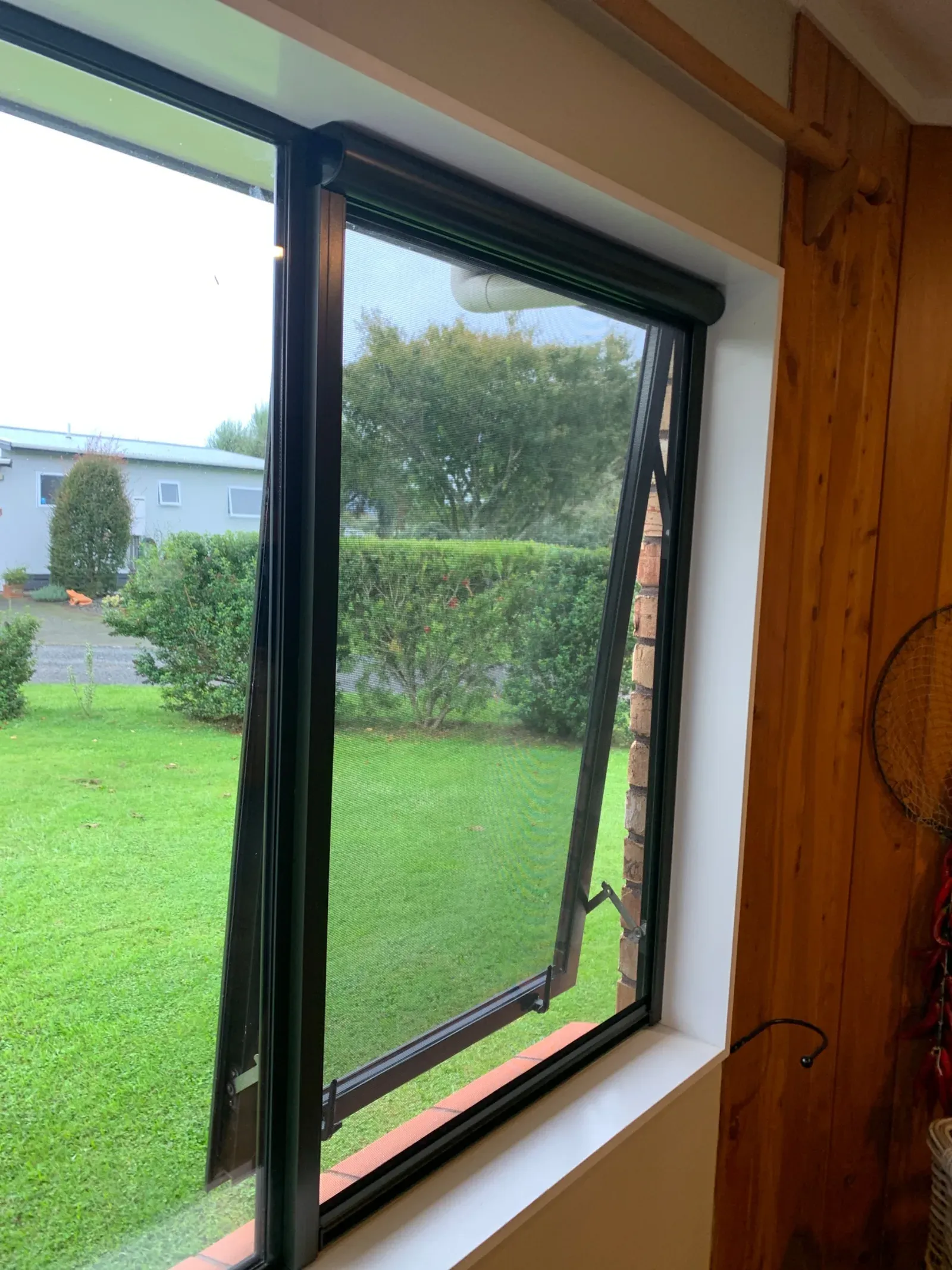 Black Serene retractable screen fitted to an awning window in a timber-lined room overlooking the garden