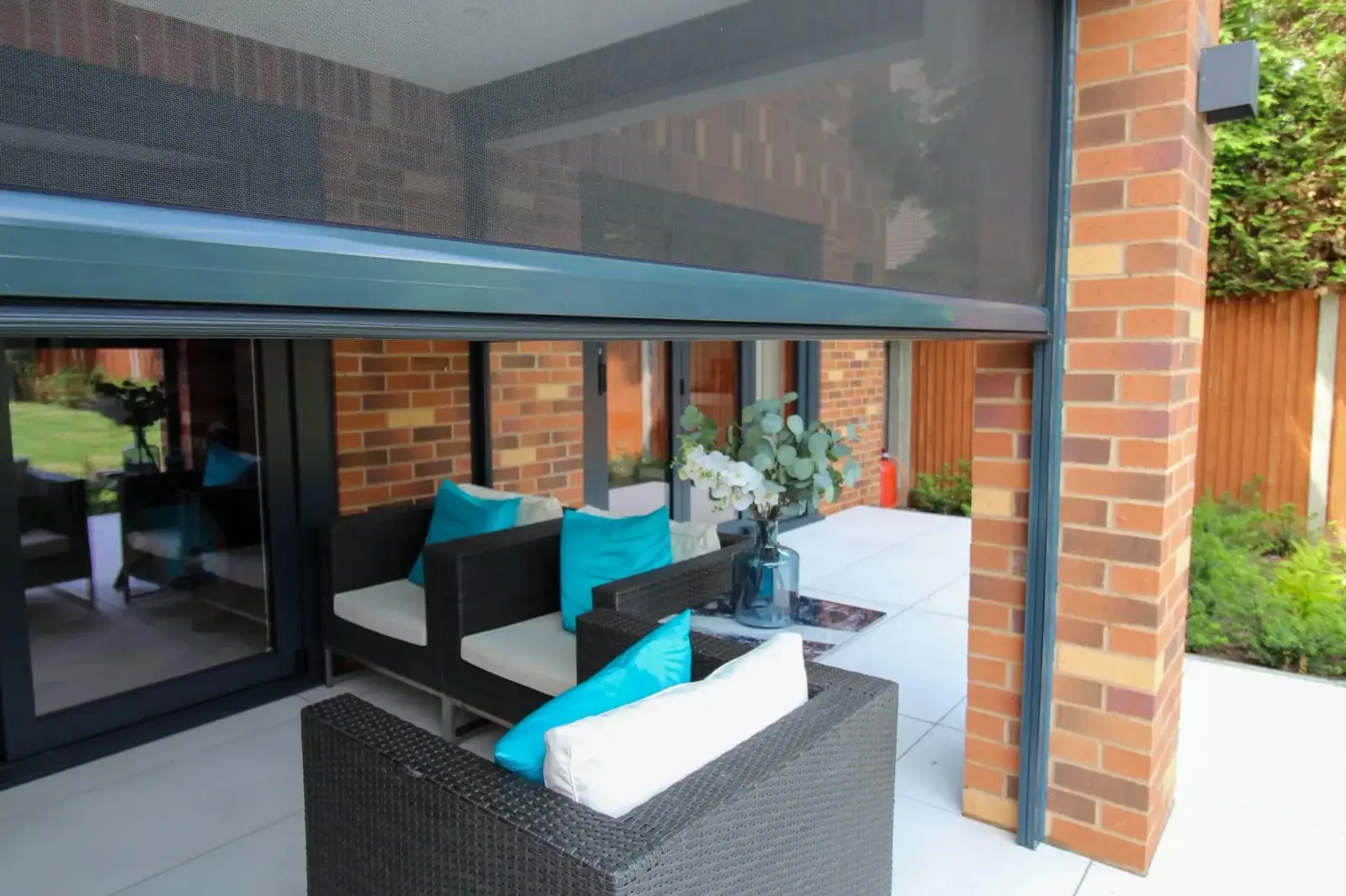 A dark outdoor mesh screen drawn down to enclose a covered brick patio with lounge furniture