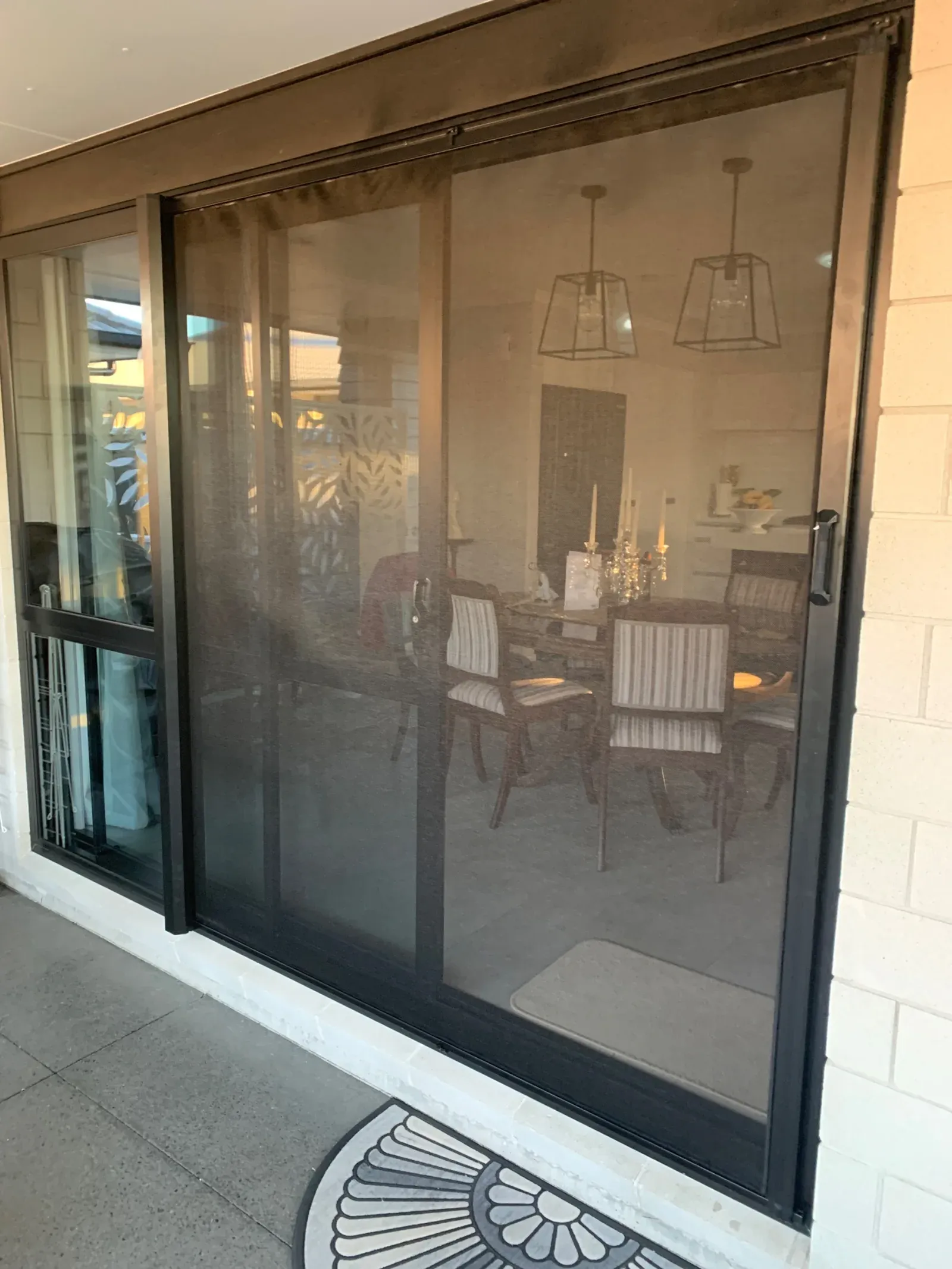A black retractable screen across a sliding door, the dining room clearly visible through the high-visibility mesh