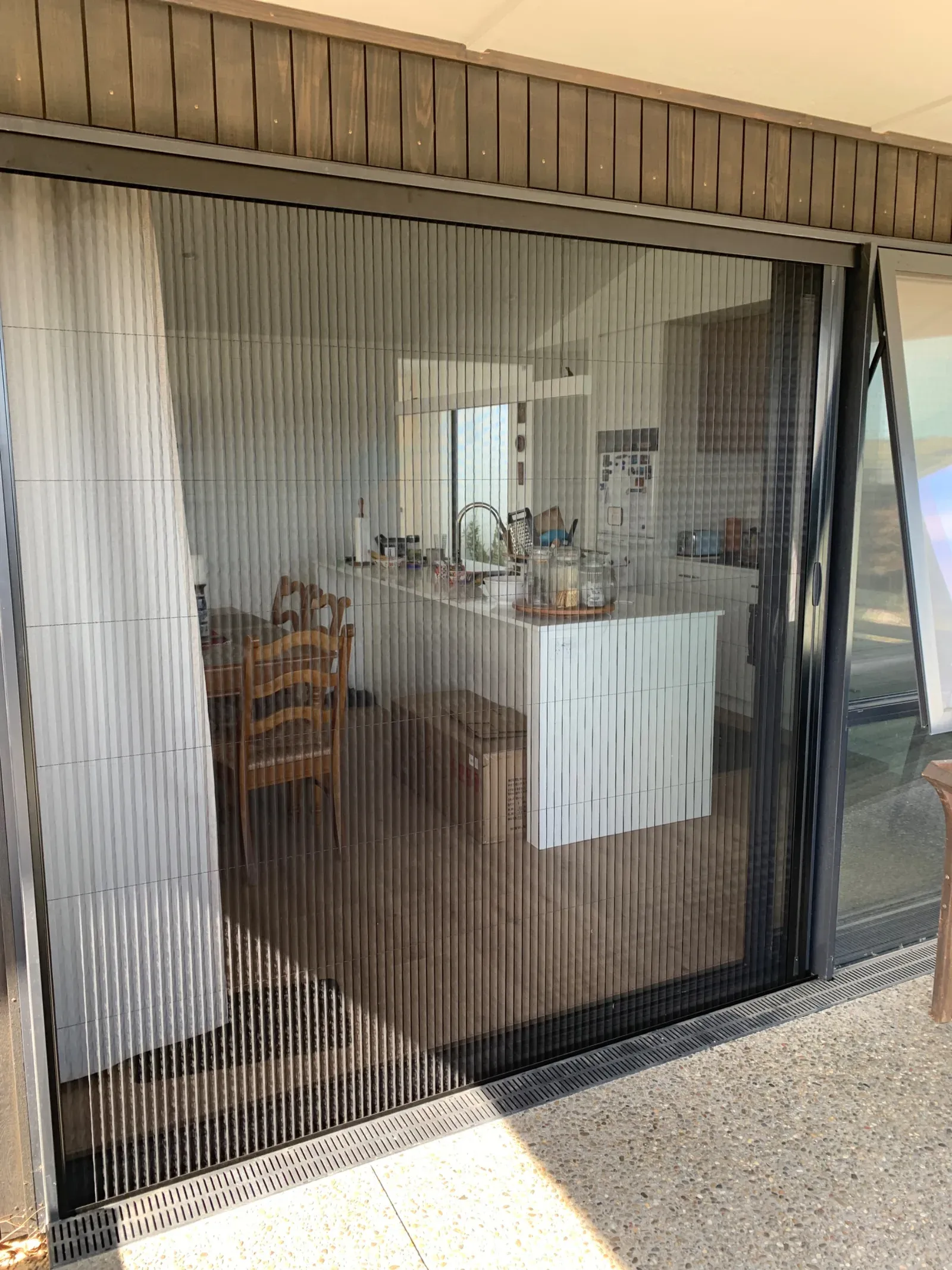 A Brio 612 pleated retractable screen drawn across a wide stacking slider into a kitchen and dining space