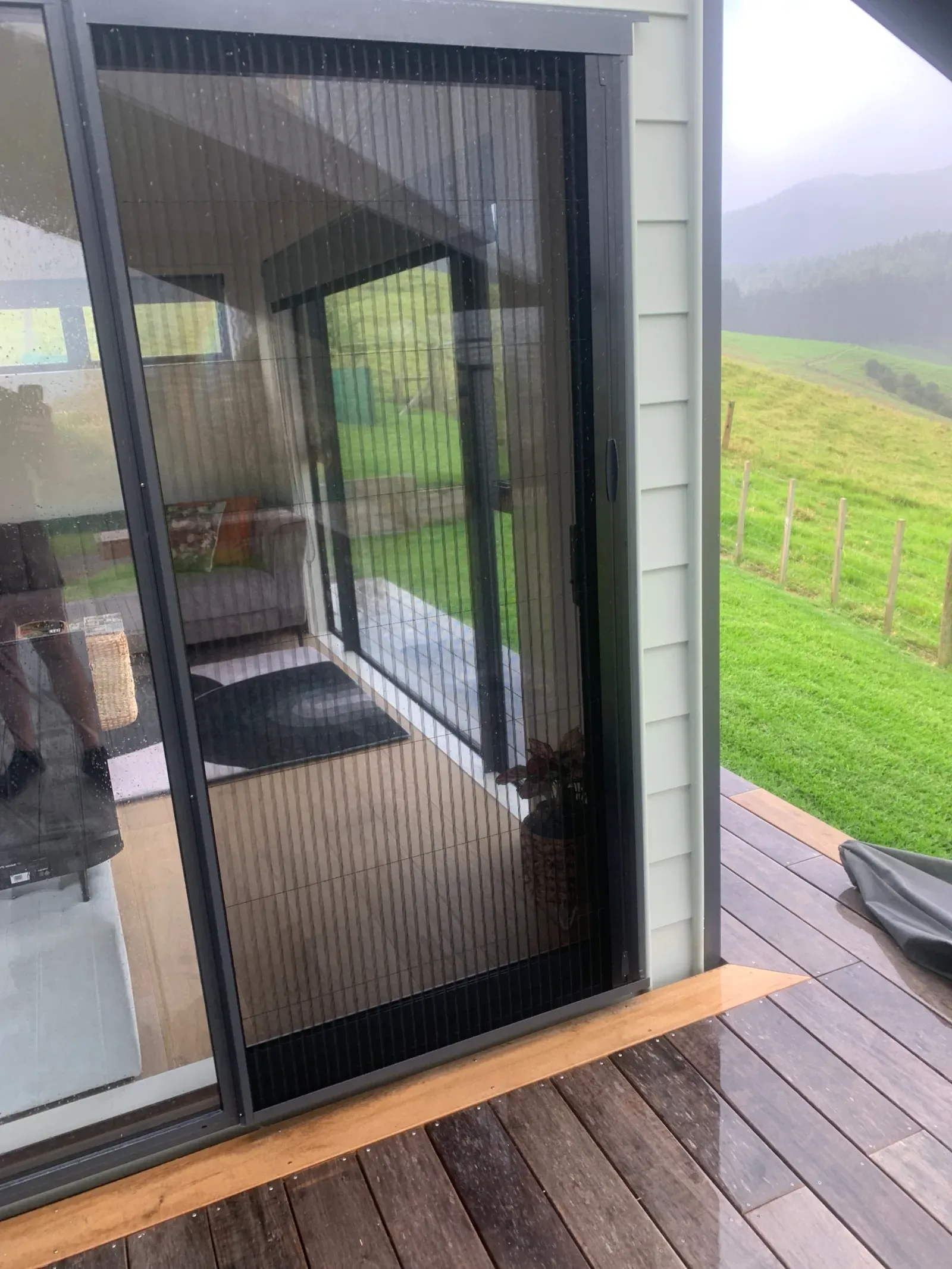 A pleated retractable door screen across a slider, looking out to green Coromandel hills