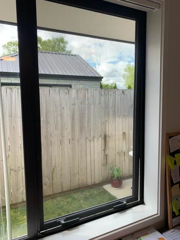A magnetic insect screen fitted over a black-framed window looking out to a timber fence and garden