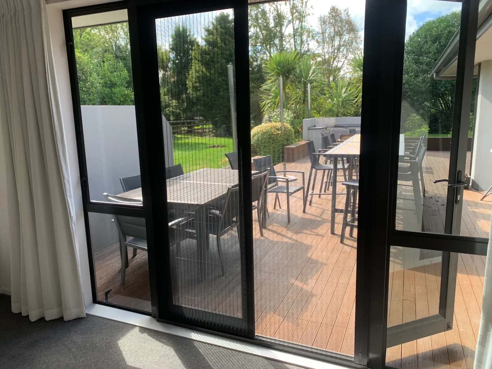 Inside view through a black Brio 612 pleated screen on a sliding door onto a deck with outdoor dining