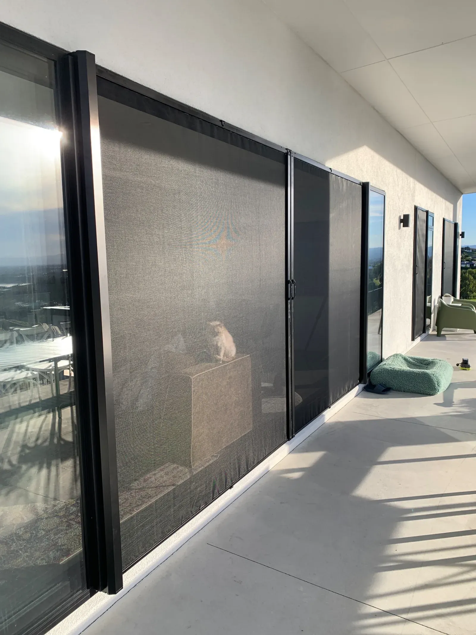Black-framed retractable Wall Screens drawn along a covered patio of sliding doors at a modern hillside home