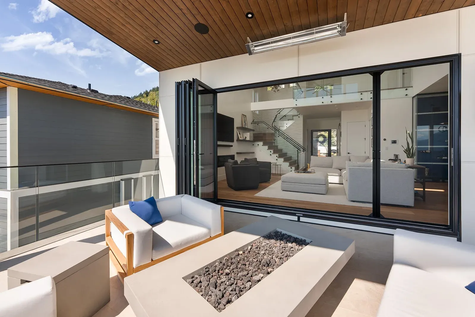 Wide bi-fold doors folded right back onto a modern outdoor deck with a fire-pit lounge