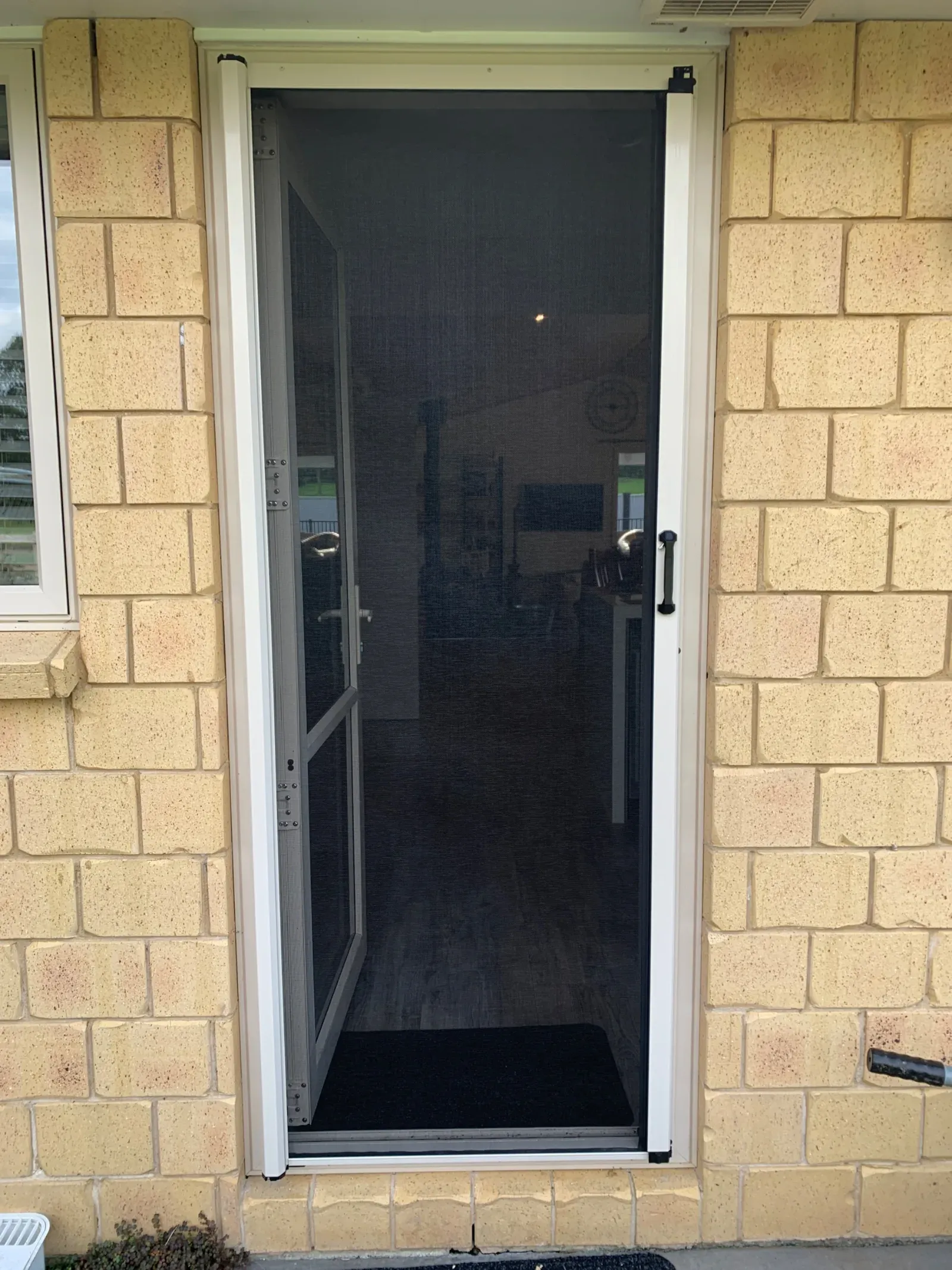 Black retractable MeshLock screen on a single front door of a cream brick home, viewed from the entry