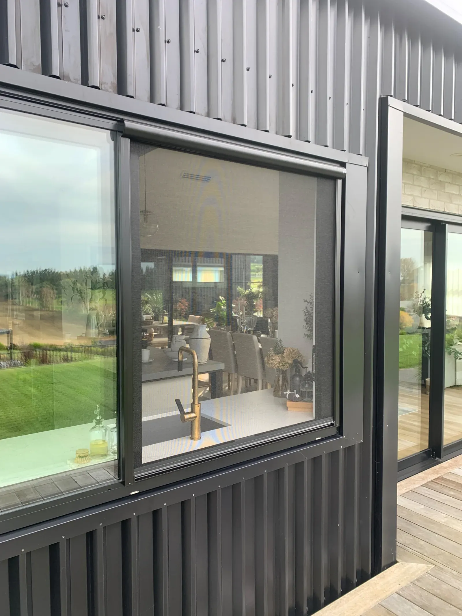 Black Serene retractable screen outside-fitted to a kitchen slider window on a dark metal-clad home