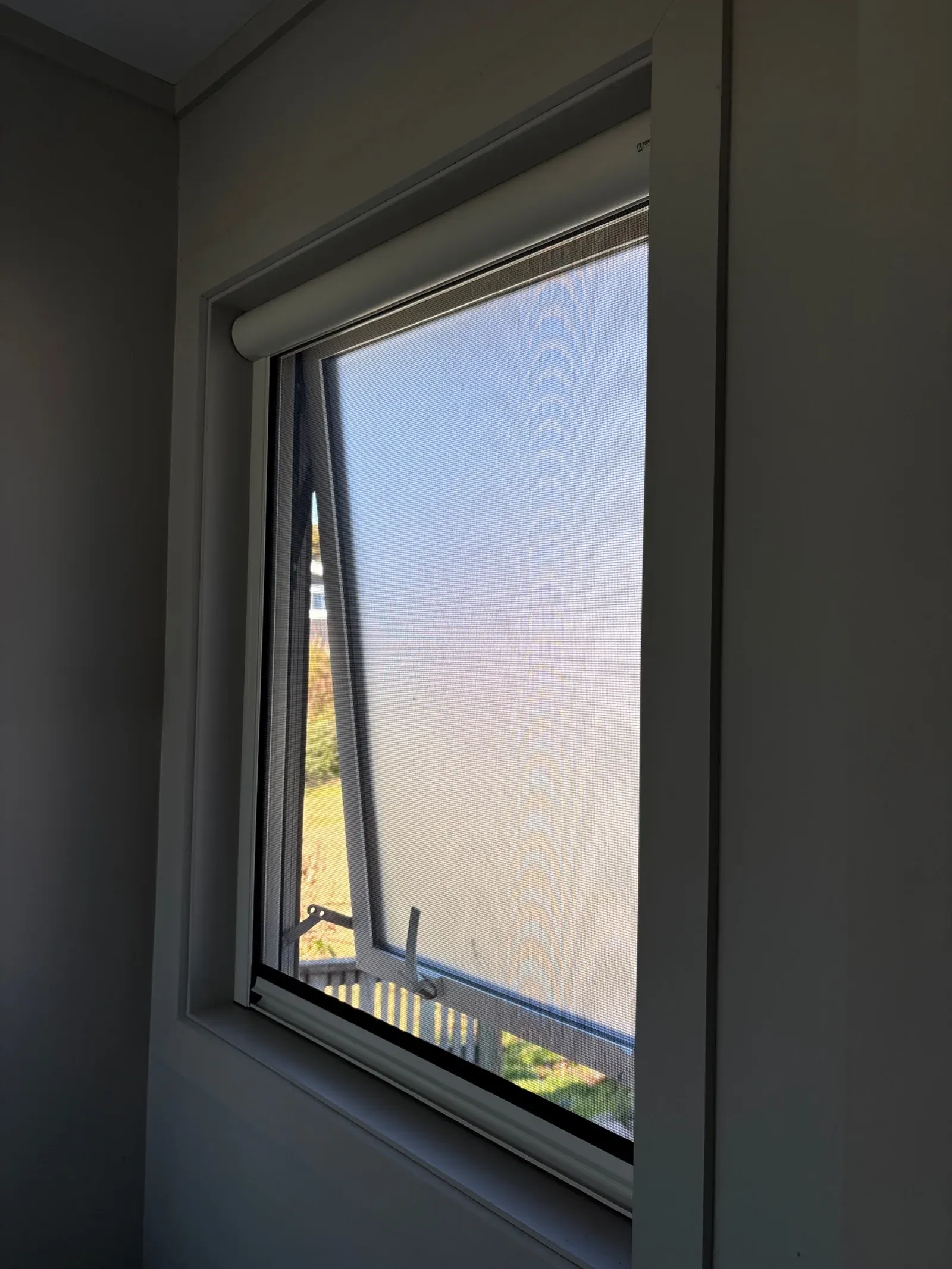 White Serene retractable screen drawn down over an awning window cranked open to a garden