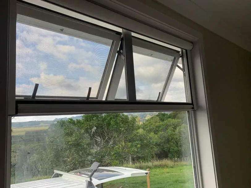 Two awning windows wound open behind retractable insect screens, looking over a rural valley