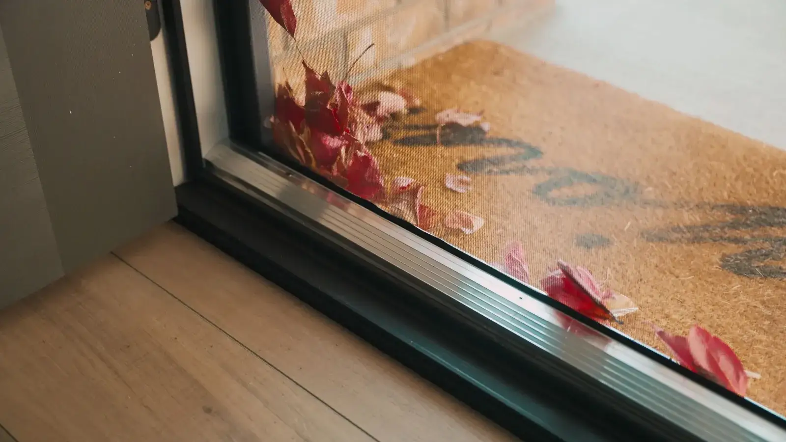 Close-up of a retractable screen door's bottom rail, the mesh held captured in its track on a timber floor