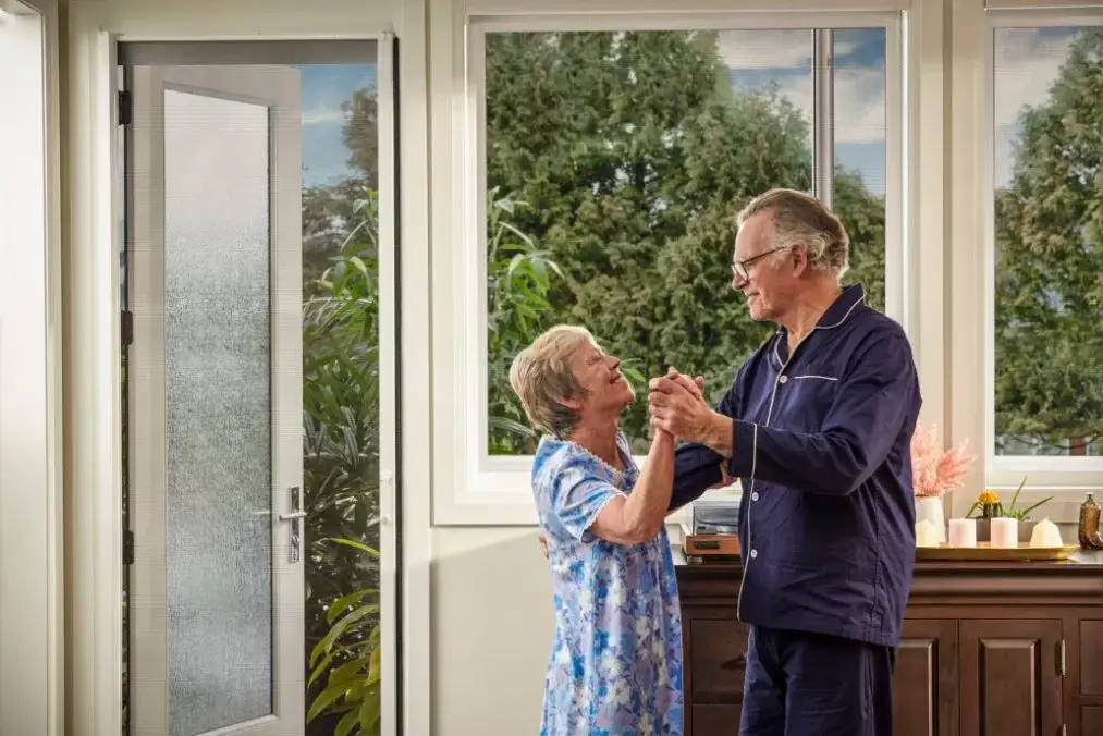 An older couple dancing in a bright living room beside a Phantom retractable screen door