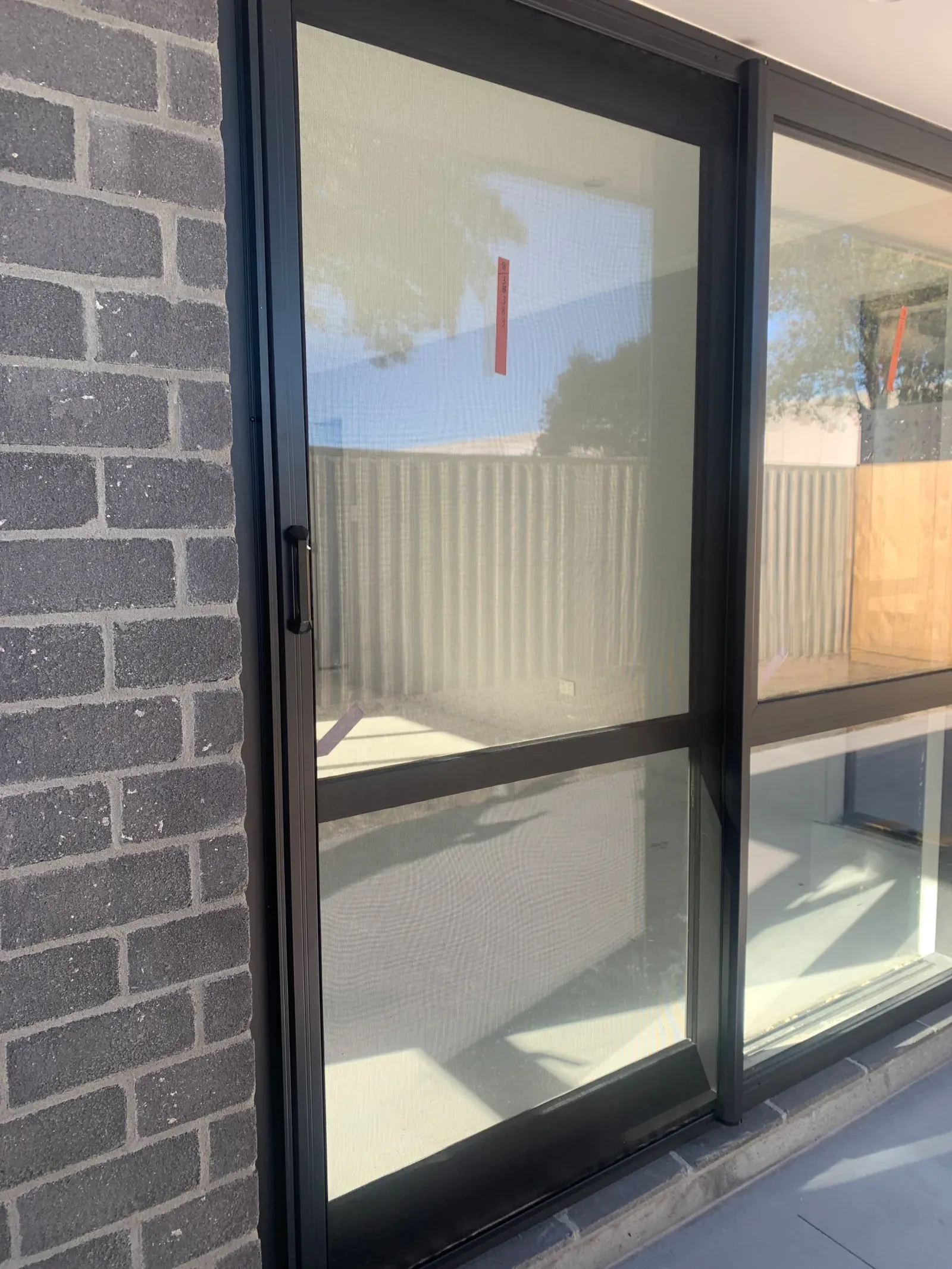 A black-framed sliding insect screen door fitted across a ranch slider on a grey-brick new build