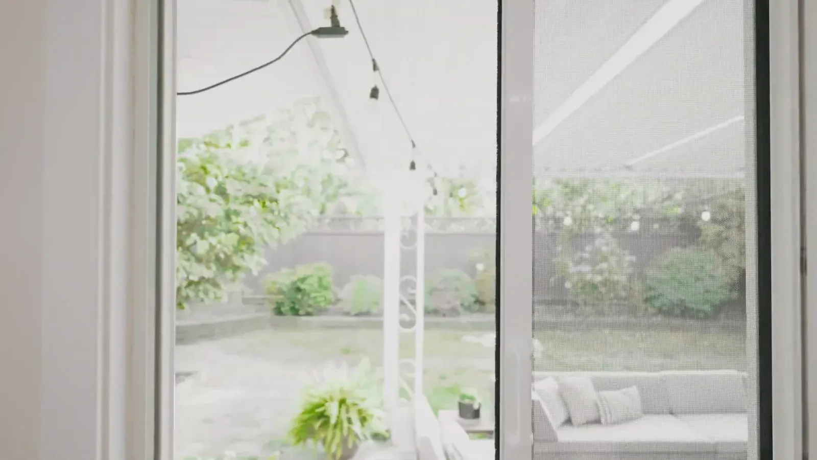MeshLock retractable screen closed across a single patio door, with the garden visible through the mesh