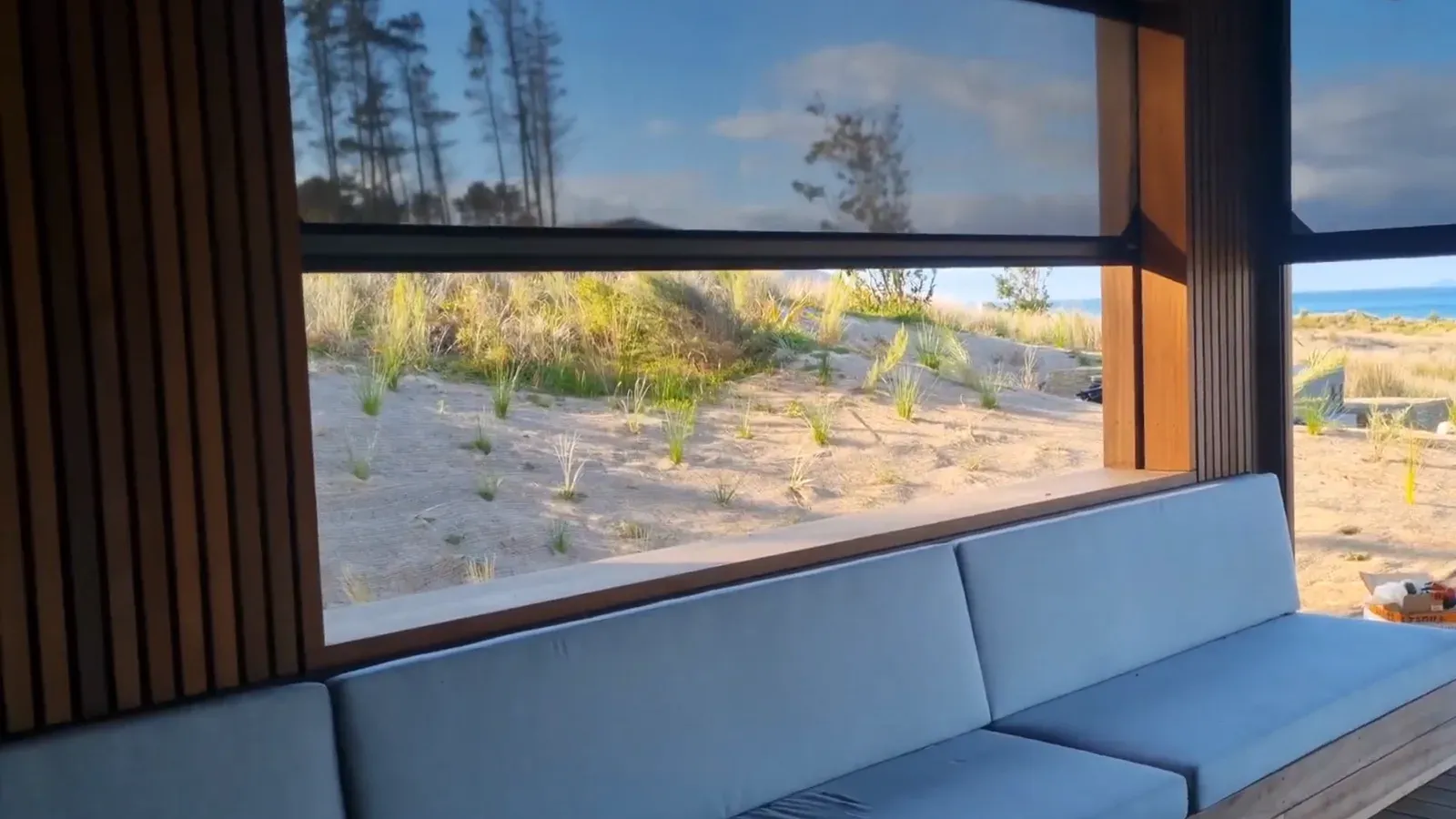 An Executive screen drawn down across a covered deck opening at Tara Iti, looking through the mesh to marram dunes and the sea