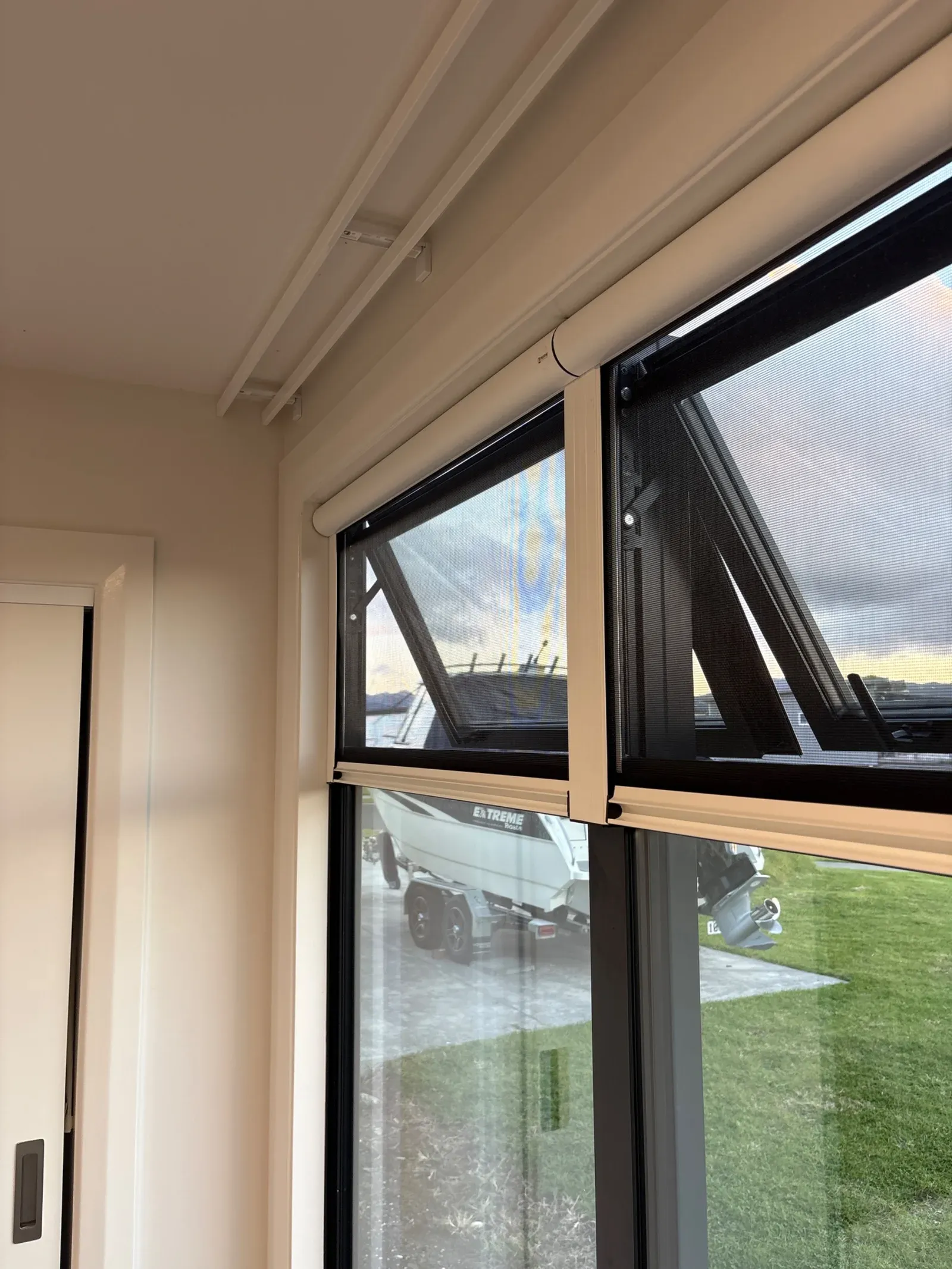 Twin awning windows fitted with retractable insect screens, looking over a coastal lawn